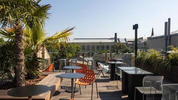 An outdoor patio with tables and chairs, surrounded by plants and a palm tree.