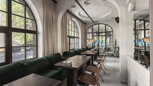 A modern restaurant with high arched windows, green upholstered seating, and wooden tables. - BRYK Hotel (Odesa)