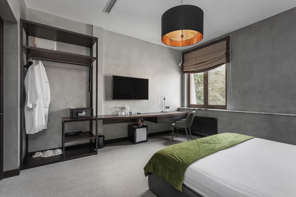 A modern hotel room with a bed, a desk with a chair, a television, a wardrobe, and a window with curtains.