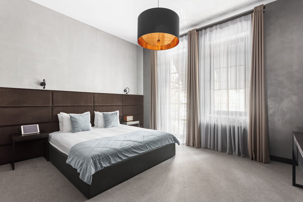 A modern bedroom with a large bed, a bedside table with a lamp, and sheer curtains.