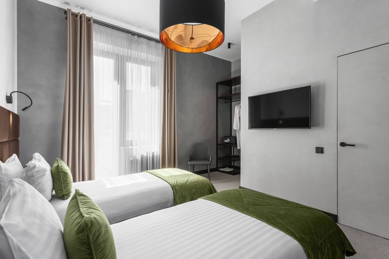 Habitación de hotel con dos camas, televisión, armario y un amplio ventanal con cortinas.