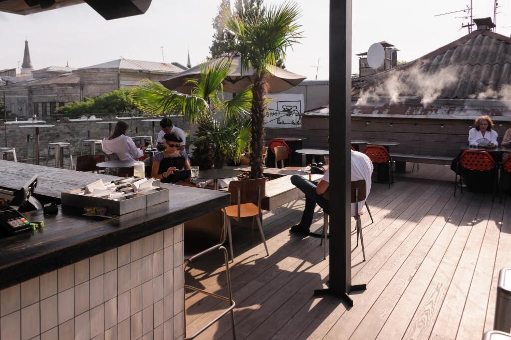 An outdoor dining area with wooden flooring, tables, chairs, and a counter with a cash register.