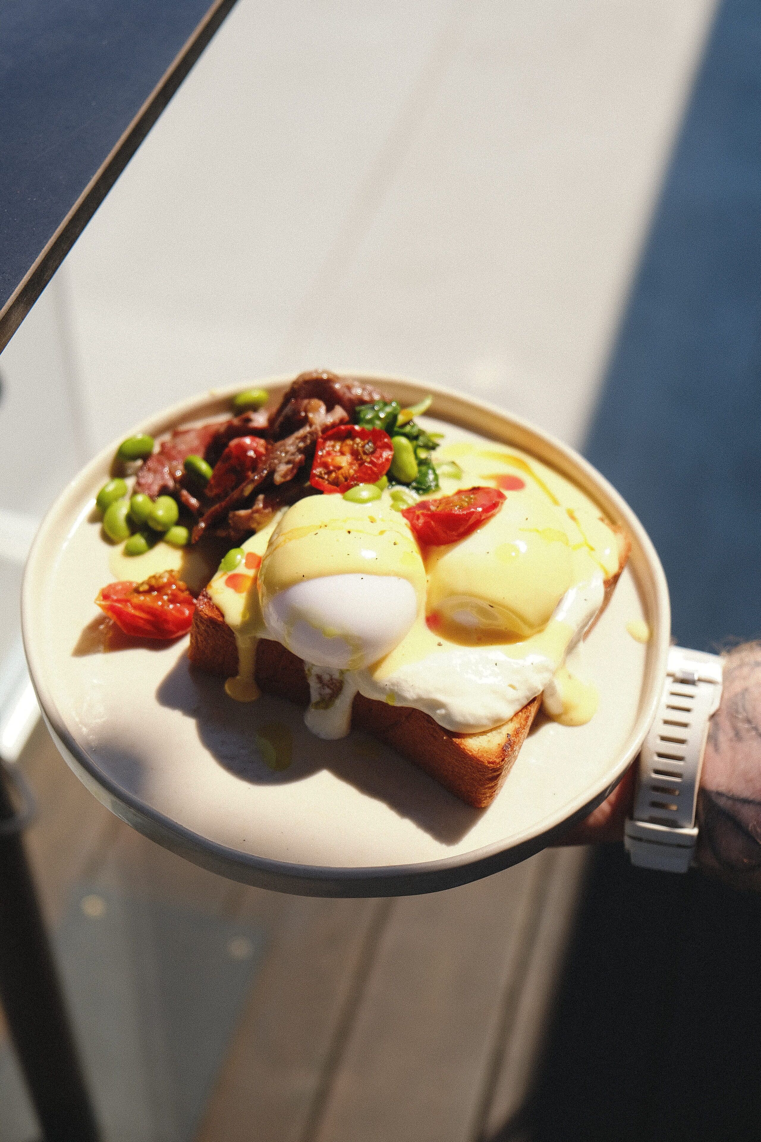A plate of food with eggs benedict, green peas, tomatoes, and bacon.