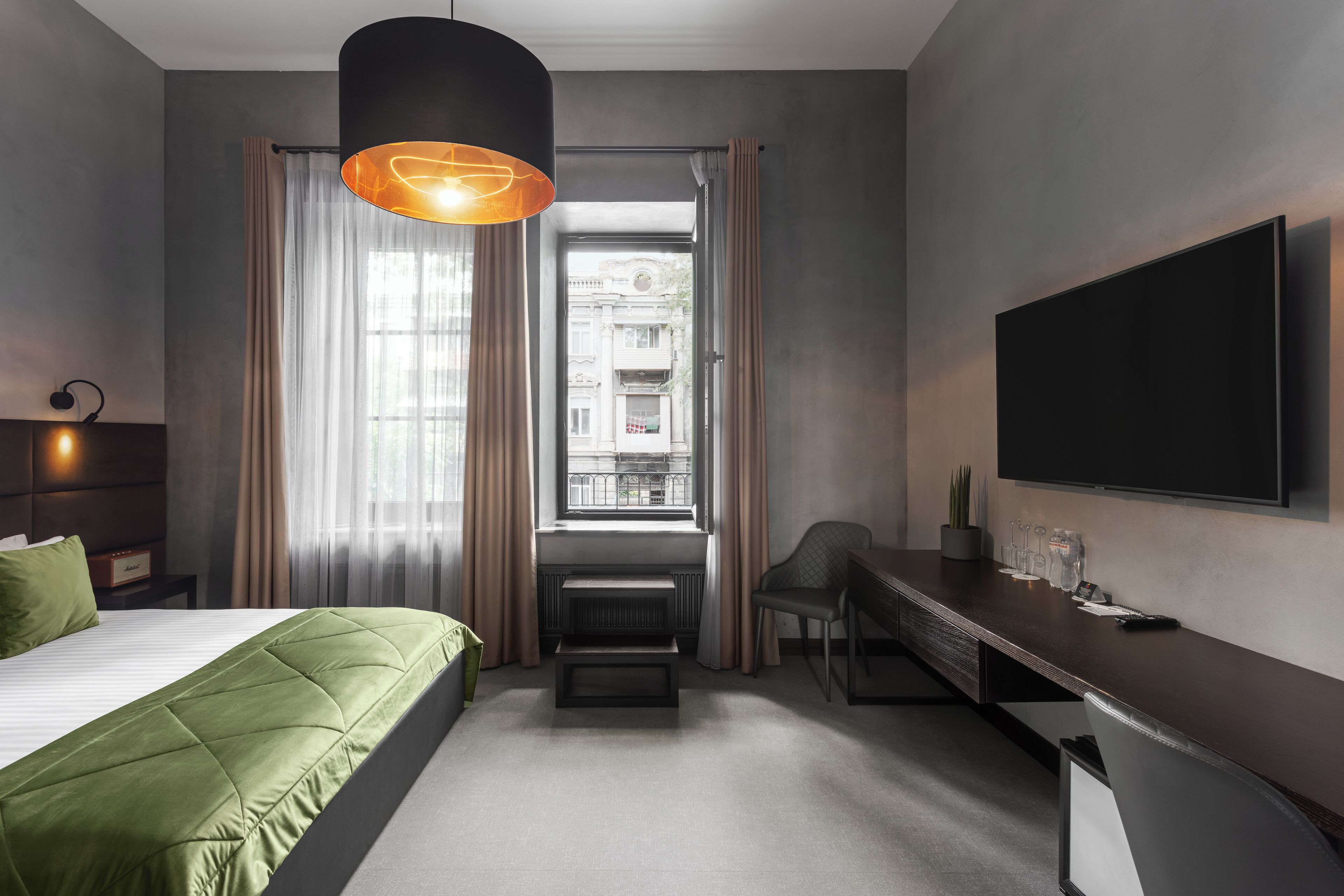 A modern hotel room with a large bed, a desk, a chair, a television, and a window with curtains.