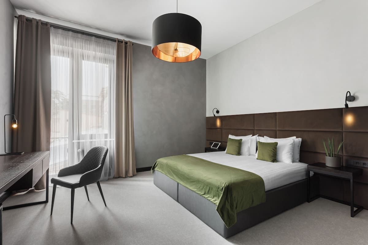 A modern hotel room with a large bed, a desk, a chair, and a hanging light fixture.