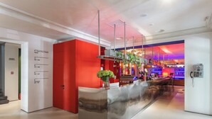 A modern reception area with a red accent wall, a stainless steel counter, and a bar area with ambient lighting. - BRYK Hotel (Odesa)