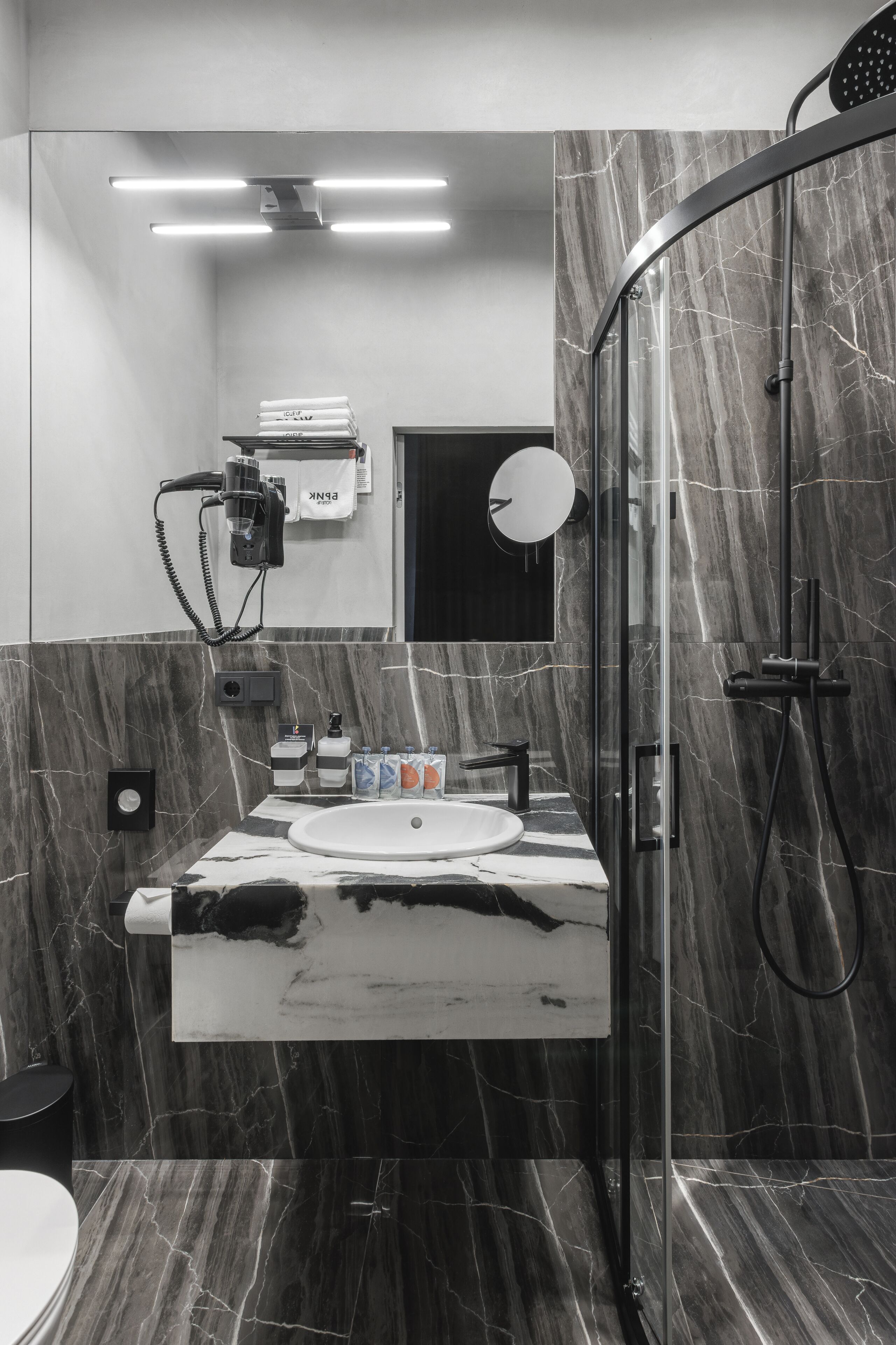 Ein modernes Badezimmer mit einer gläsernen Duschkabine, einem Marmorwaschbecken und einem Handtuchhalter mit gefalteten Handtüchern.
