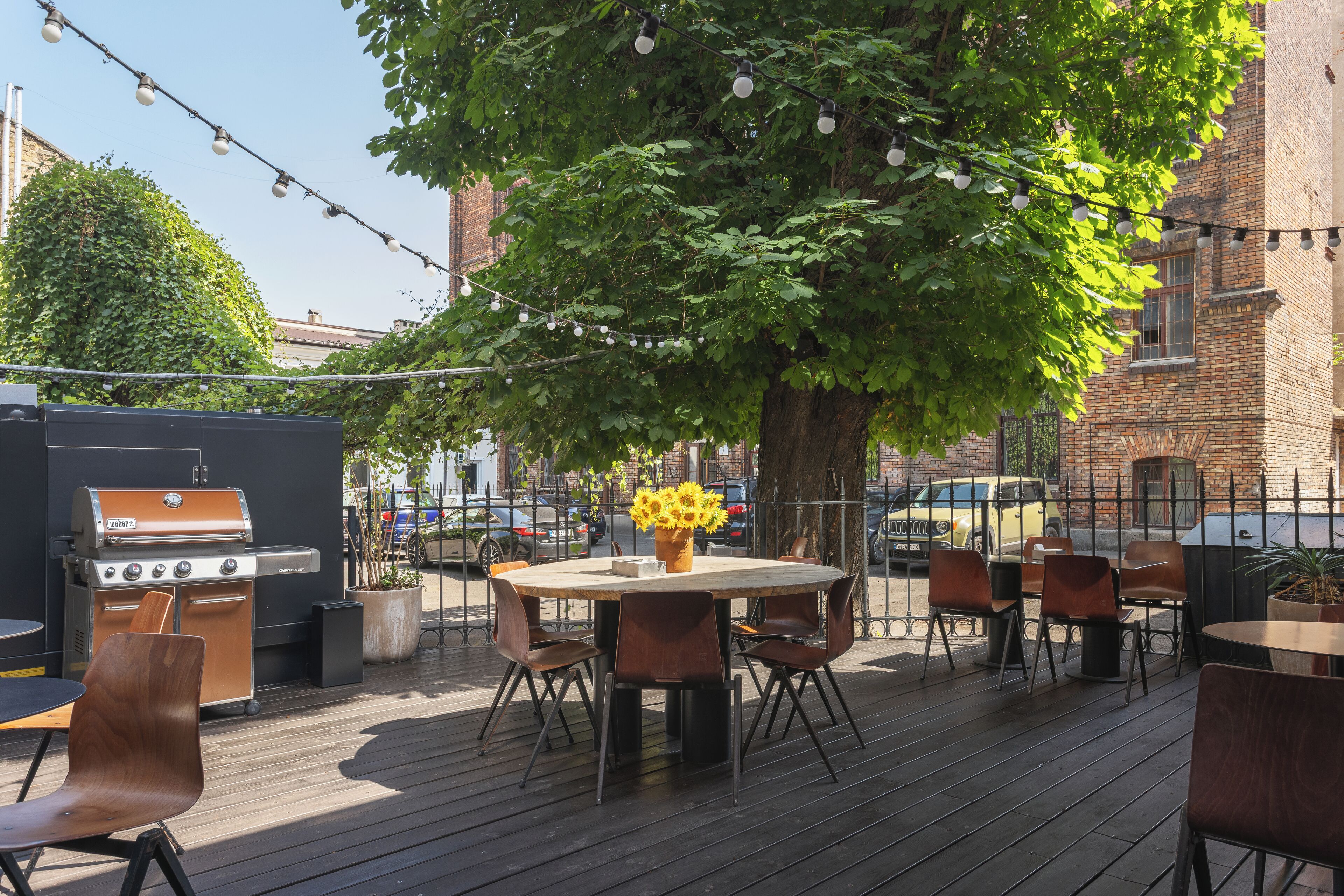 An outdoor patio with a round table, chairs, a grill, and string lights.
