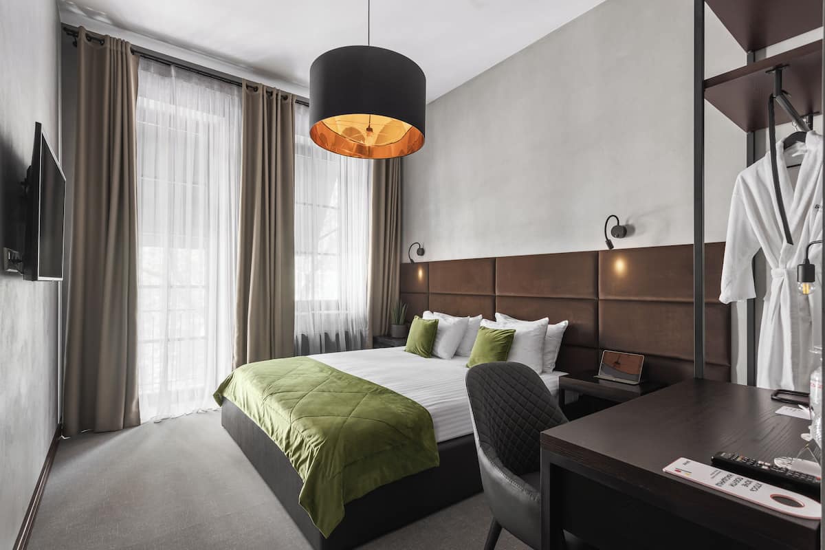 A hotel room with a bed, a desk, a chair, a robe, and a hanging light fixture.