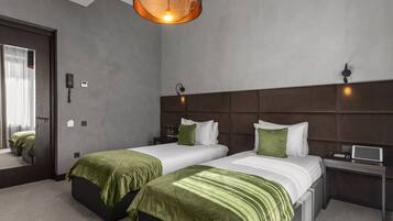 Una habitación de hotel moderna con dos camas, un espejo grande, una mesita de noche con lámpara y un aplique de techo.