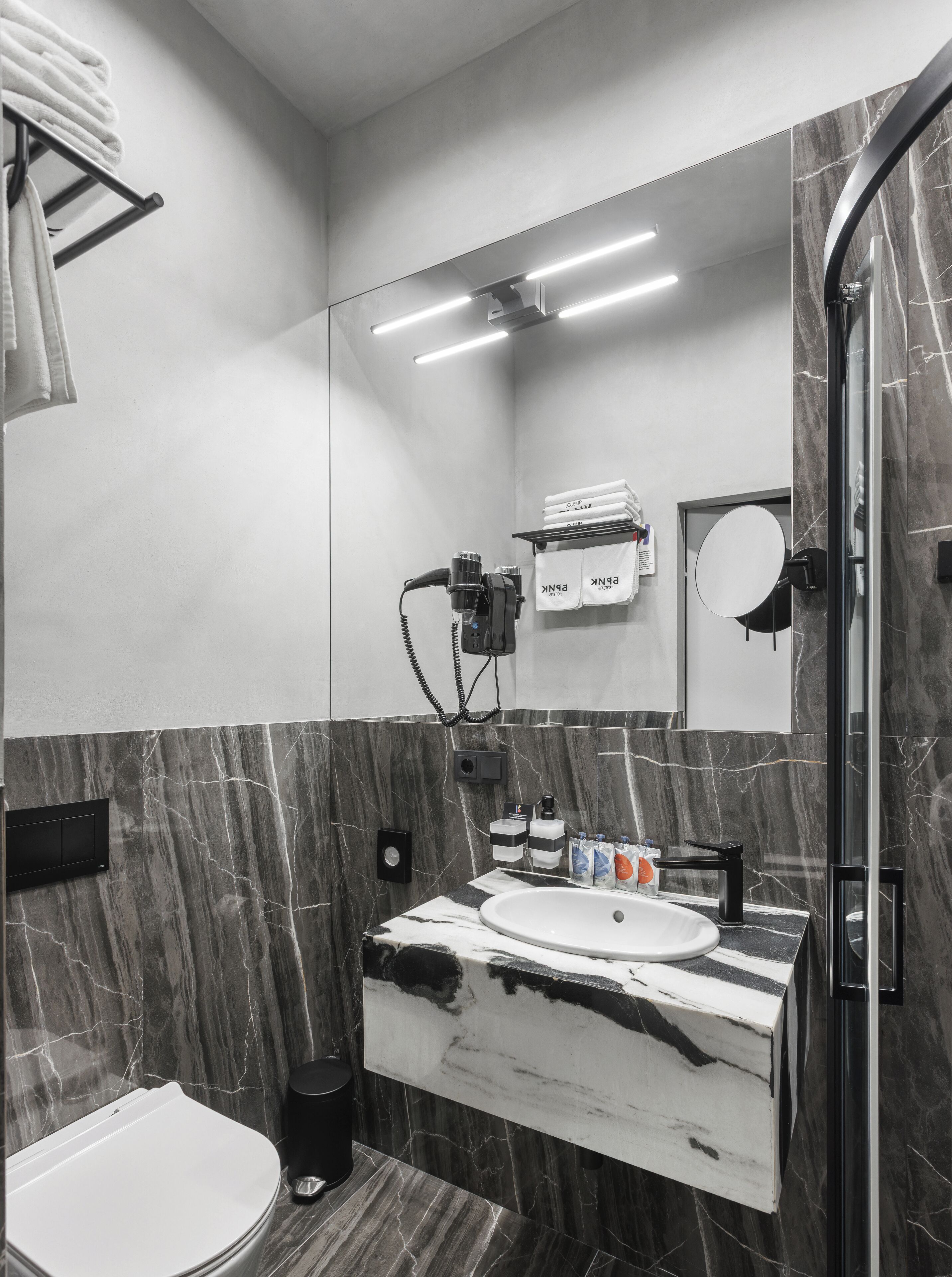 A modern bathroom with a marble vanity, a toilet, a shower with a glass door, and a towel rack with folded towels.