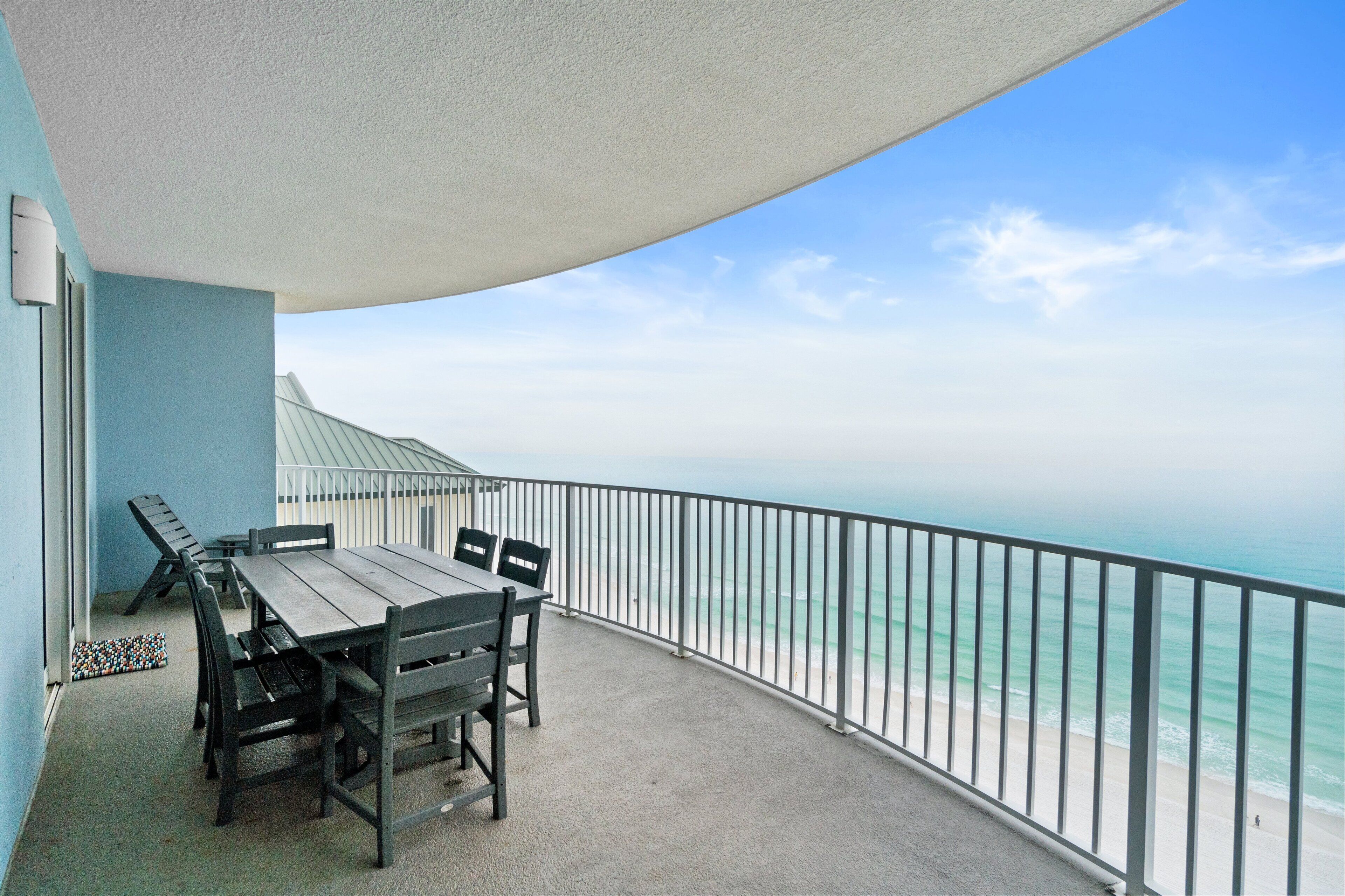 A balcony with a table and chairs, overlooking a beach.