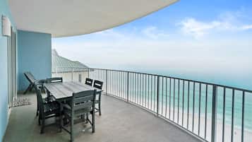 A balcony with a table and chairs, overlooking a beach.