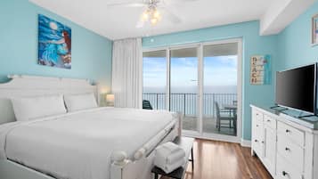A bedroom with a bed, a ceiling fan, a TV, and a balcony with a view of the ocean.