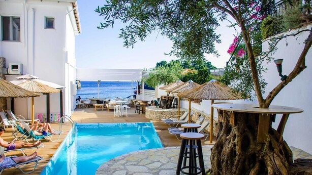 A poolside area with lounge chairs, umbrellas, and a tree trunk table. - Bianco Resort - Adults Only (Parga)