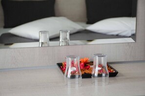 A hotel room with a bed, a mirror reflecting the bed, and two clear glass vases on a table with flowers. - Bianco Resort - Adults Only (Parga)