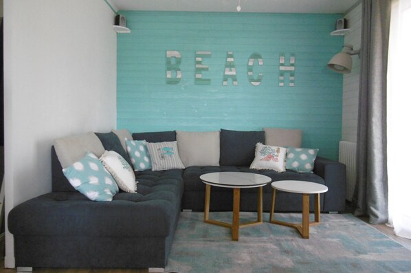 A living room with a teal accent wall, a sectional sofa, and two small tables.