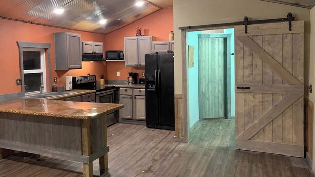 A kitchen with a central island, built-in appliances, and a sliding barn-style door. - Secluded Ranch House Cabin in Eminence - Ozarks @ Old Desperado Ranch (Eminence)