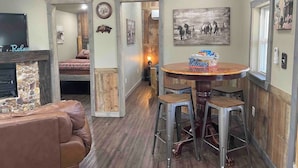 A cozy living area with a fireplace, a round wooden dining table with bar stools, and a television. - Secluded Ranch House Cabin in Eminence - Ozarks @ Old Desperado Ranch (Eminence)