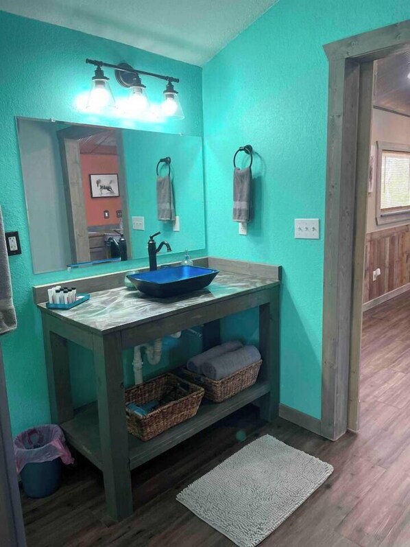 A bathroom with a blue sink, a mirror, and a shelf with baskets.