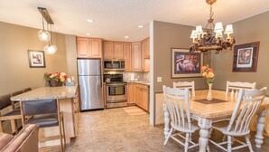 A kitchen with wooden cabinets, stainless steel appliances, a dining table with chairs, and a chandelier. - Pine Ridge Incline Condo: Ski-In, Walk To Downtown (Breckenridge)