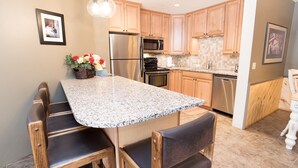 A kitchen with granite countertops, wooden cabinets, stainless steel appliances, and a dining area with wooden chairs. - Pine Ridge Incline Condo: Ski-In, Walk To Downtown (Breckenridge)