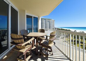 Ein Balkon mit Tisch und Stühlen mit Blick auf einen Strand und ein Hochhaus.