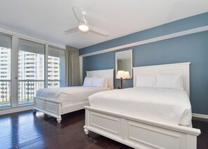 A hotel room with two beds, a ceiling fan, a large window with a view of buildings, and a mirror on the wall. - Beachfront chic 3-bed, 3-bath w/private balcony in Destin! 🌺🌴💙 (Destin)