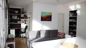 Ett modernt sovrum med en säng, en grå soffa, ett skrivbord med en dator och en bokhylla.