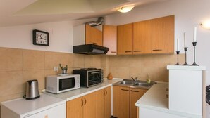 A compact kitchen with wooden cabinets, a microwave, a toaster, a kettle, and a sink. - Apartment Lala (Dubrovnik)