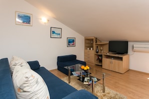 A modern living room with a blue sofa, a glass coffee table, and a television on a wooden cabinet.
