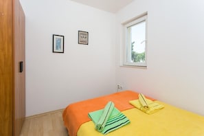 A small, bright room with a single bed, a window, and two framed pictures on the wall.