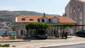 A stone building with a tiled roof, a parked car, and a scooter in front. - Apartment Lala (Dubrovnik)