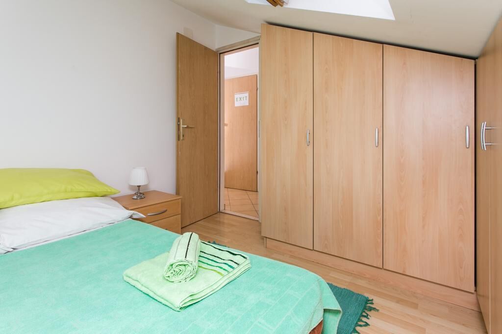 A bedroom with a bed, a nightstand, a wardrobe, and an exit sign.