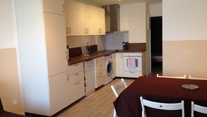 Ett kompakt kök med vita skåp, en tvättmaskin och en matplats med ett bord och stolar.