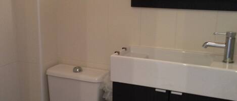 Un baño con inodoro, lavamanos y un cubo de basura.