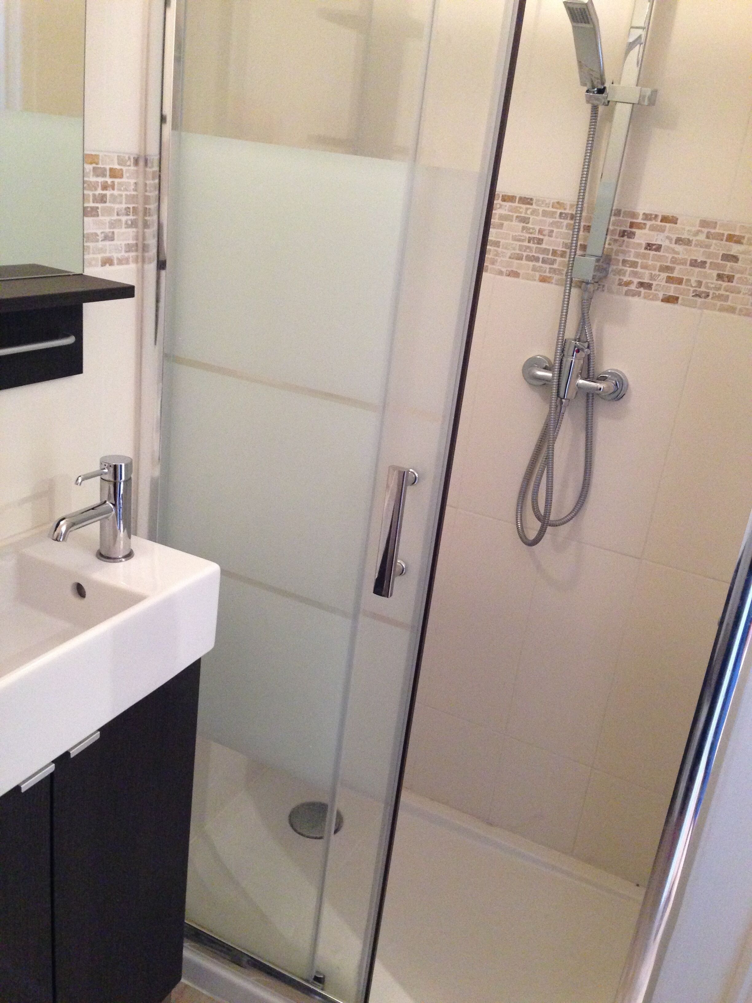 Une salle de bain moderne avec une douche à parois de verre, un lavabo blanc et un plan de toilette noir.