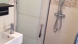 Ett modernt badrum med en dusch som är avskärmad med glasväggar, en vit tvättställ och en svart bänkskiva.