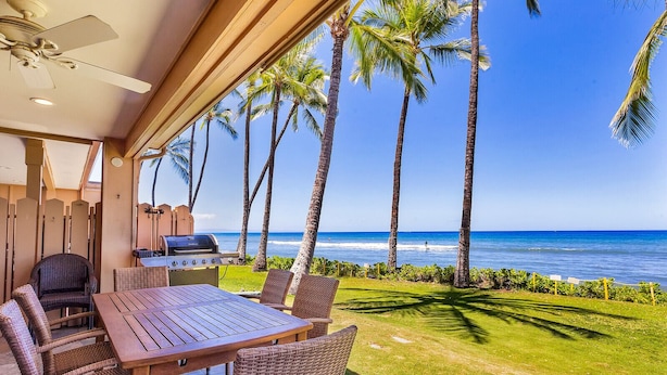 Een terras met een tafel en stoelen, een barbecue, en uitzicht op de oceaan met palmbomen.