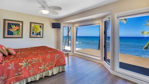 Een slaapkamer met een groot bed, een plafondventilator en uitzicht op de oceaan door een schuifdeur.