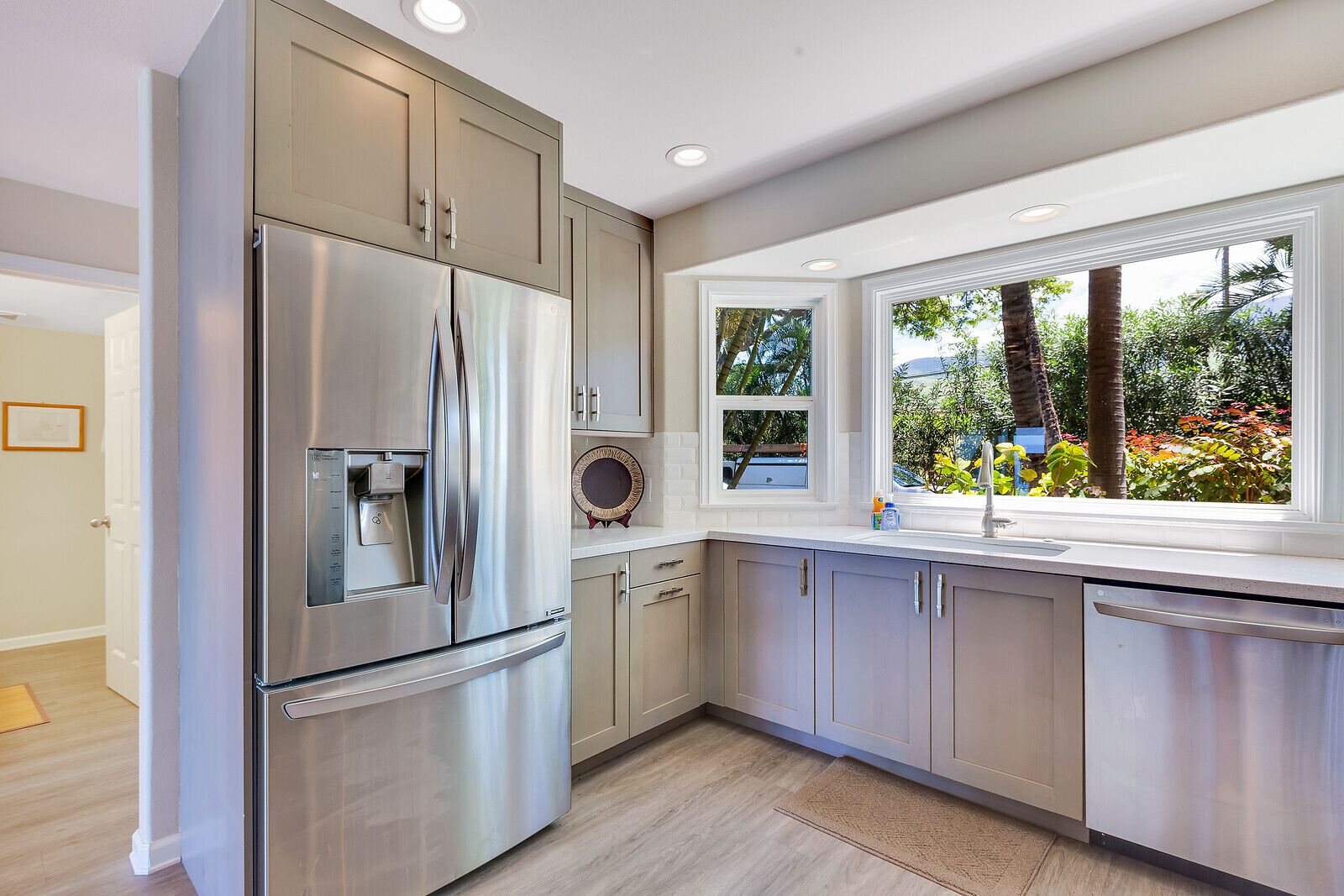 A modern kitchen with stainless steel appliances, light wood cabinets, and a large window offering a view of the outdoors.
