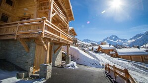 Un chalet in legno con fondamenta in pietra, balconi in legno e vista sulle montagne innevate.