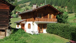 A wooden house with a balcony, surrounded by greenery and mountains in the background. - Chalet Le Roitelet (Evolène)