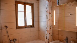 A bathroom with a bathtub, a sink, a window, and a shower. - Chalet Le Roitelet (Evolène)