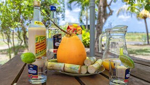 Una mesa de madera con diversas bebidas y frutas, incluyendo una botella de ron, una jarra y una naranja grande.