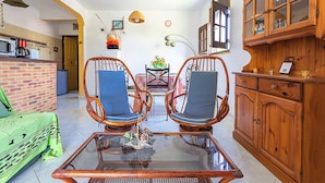 Un comedor con dos sillas de mimbre, una mesa de vidrio y un mueble de madera con puertas de cristal.