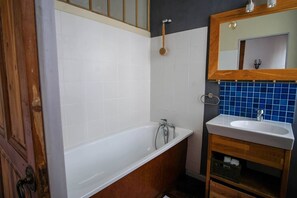 Um banheiro com banheira branca, toucador de madeira com pia e parede revestida em azulejos azuis.