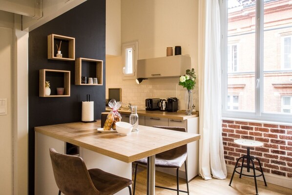 A modern kitchen with a wooden table, chairs, and a window with a view of a brick building.