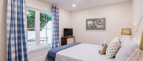 Un dormitorio con cama, televisor, un cuadro y una ventana con cortinas.