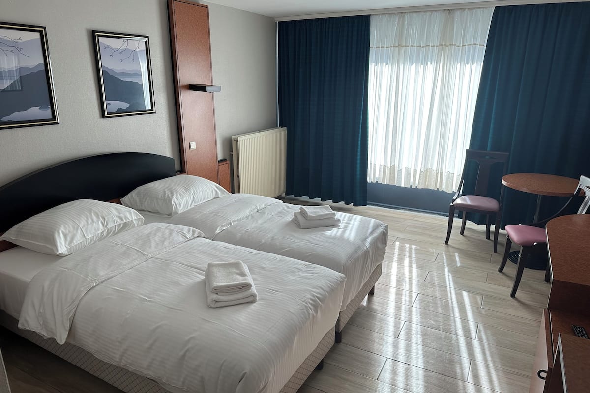 A hotel room with two beds, a desk, a chair, and a window with curtains.